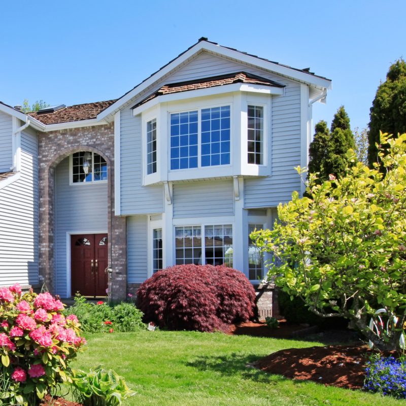 Large American grey house front exterior with green landscape.